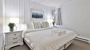 Ein aufgeräumtes Schlafzimmer mit Bett, Nachttischen, Fenster mit Vorhängen und einem gerahmten Kunstwerk.
