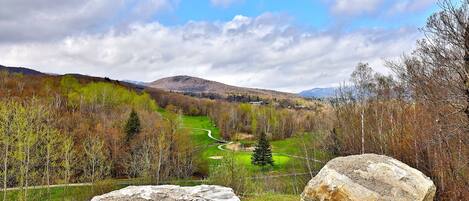 A landscape with a golf course, large rocks, and a mountainous background.
