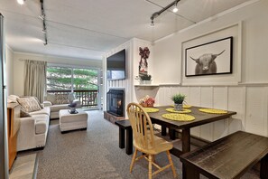 Un salon moderne avec une cheminée, une table à manger avec des sets de table jaunes, un canapé et un téléviseur fixé au mur.