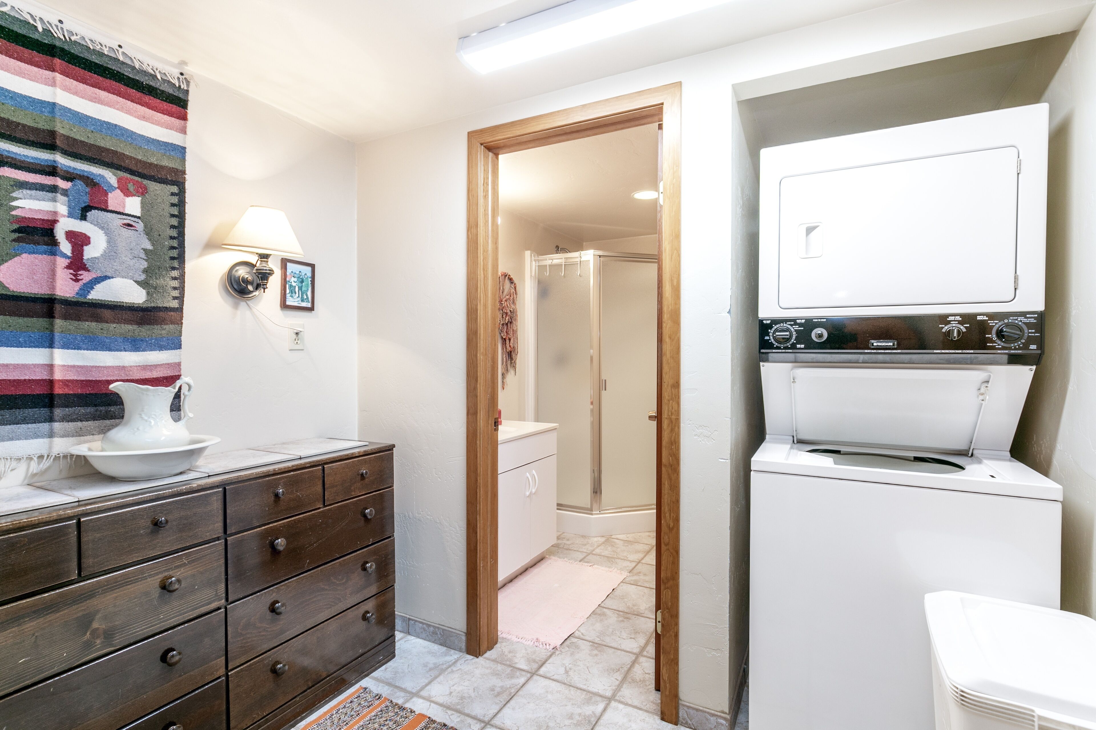 A bathroom with a wooden vanity, a white washing machine, and a shower area.