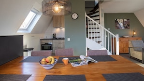 Een eethoek met een houten tafel, een schaal fruit en een tijdschrift. Er is een trap die naar een hoger niveau leidt.