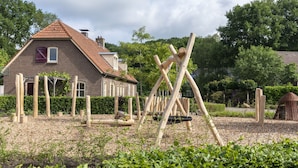Een houten schommel in een tuin, met een bakstenen huis op de achtergrond.