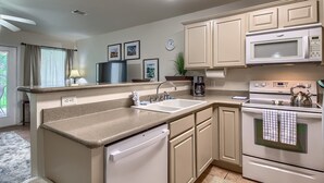 Une cuisine moderne avec des meubles de couleur beige, un lave-vaisselle encastré, un four à micro-ondes et un four traditionnel. On y trouve un évier avec un robinet, une machine à café et une horloge murale.