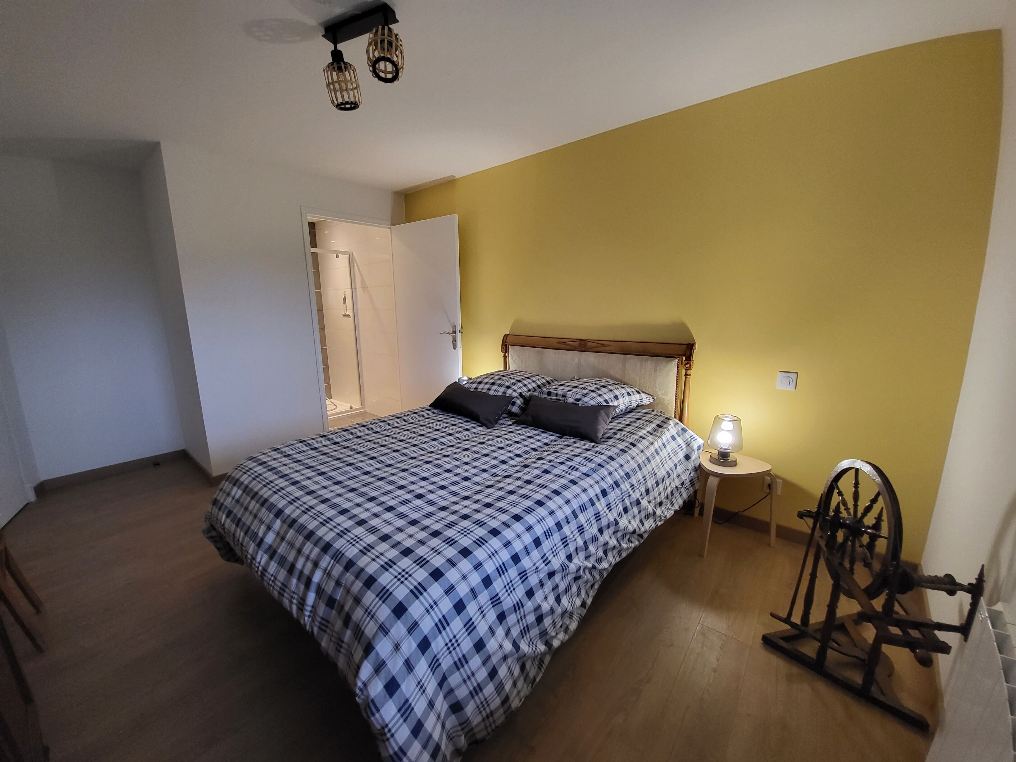 Une chambre à coucher comprenant un lit, une table de chevet, une lampe, une chaise en bois et une porte donnant accès à une douche.