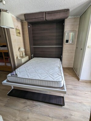 A bedroom with a bed, a nightstand, a lamp, and a wooden floor.