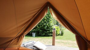 Une tente avec un lit à l’intérieur, une terrasse en bois à l’extérieur et un arbuste vert en arrière-plan.