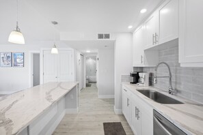 A modern kitchen with white cabinetry, a marble countertop, and stainless steel appliances.