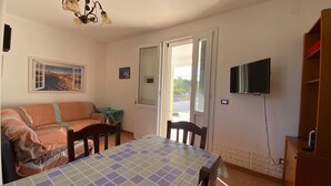 Ett rum med en soffa, ett bord med en rutig duk, en tv som är monterad på väggen och en dörr som leder ut.