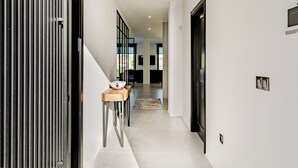 A modern hallway with a wooden side table, a black door, and a view into a dining area. - Villa Moderna con Encanto a 15 Minutos de Sevilla (Gelves)