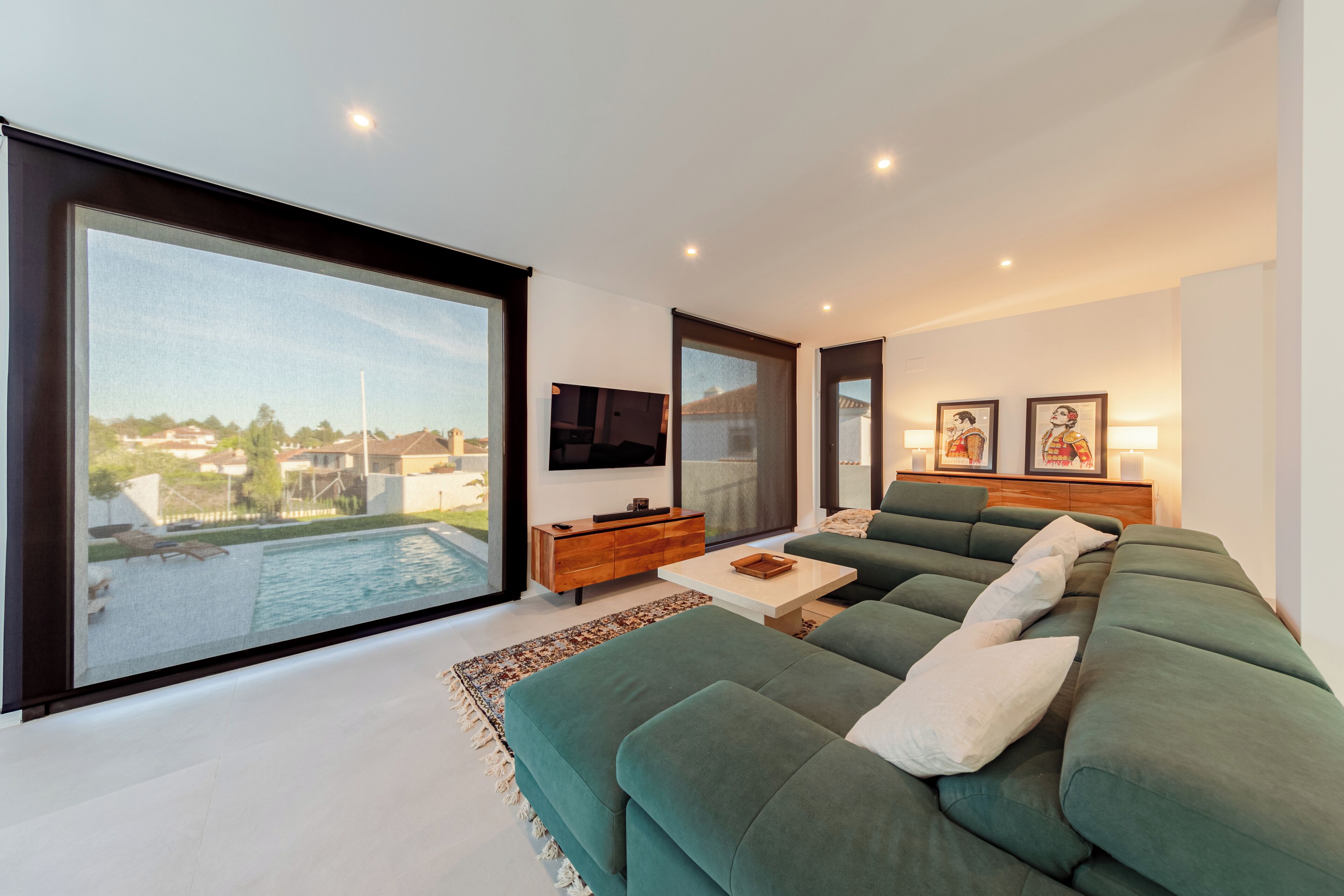 Een moderne woonkamer met een grote groene bank, een houten bijzettafeltje en een flatscreen televisie aan de muur.