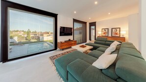 A modern living room with a large green sofa, a wooden side table, and a flat-screen TV mounted on the wall. - Villa Moderna con Encanto a 15 Minutos de Sevilla (Gelves)