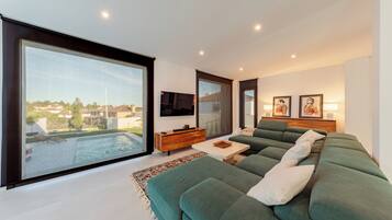 Een moderne woonkamer met een grote groene bank, een houten bijzettafeltje en een flatscreen televisie aan de muur.