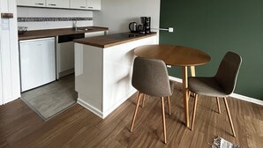A modern kitchen with white cabinets, a wooden countertop, and a coffee maker. There is a dining area with a round table and two chairs. - Charming apartment by the sea! (Wendtorf)
