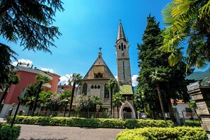 Situated in a serene garden, this historic church features a striking steeple and clock tower amidst lush greenery and palm trees.