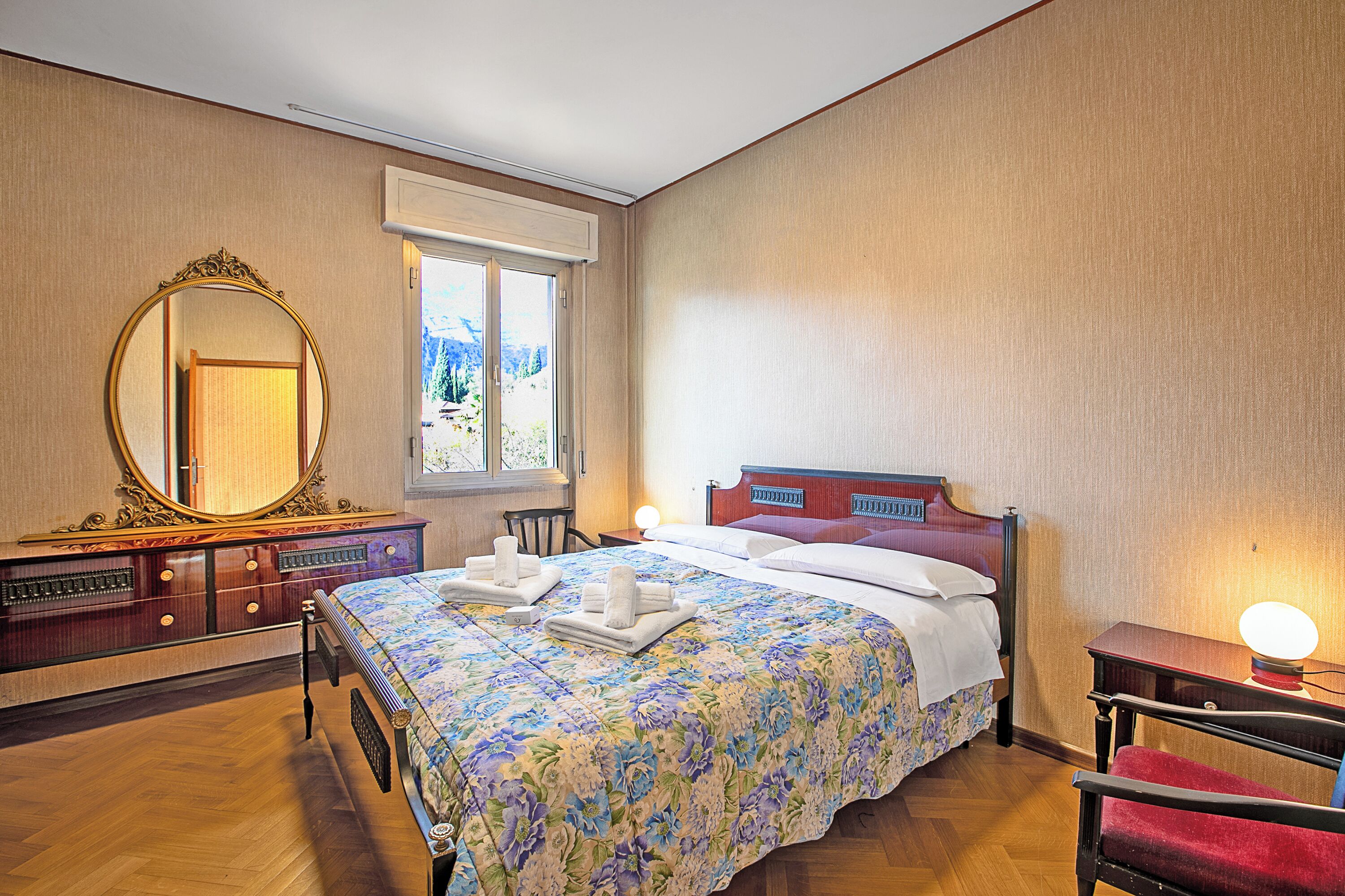 A hotel room with a large bed, a wooden dresser, a mirror, and a window with a view.