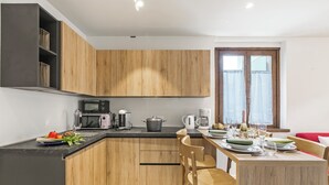 A modern kitchen with wooden cabinets, a black countertop, and a dining area with a table set for two. - Appartamento 30 Nodi Torbole 2min Walk to Lake (Nago-Torbole)