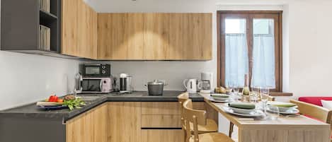 Una cocina moderna con armarios de madera, encimera negra y un comedor con mesa dispuesta para dos personas.