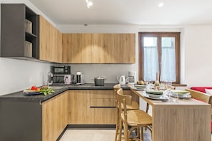 A modern kitchen with wooden cabinets, a black countertop, and a dining area with a table set for two. - Appartamento 30 Nodi Torbole 2min Walk to Lake (Nago-Torbole)