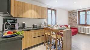 A modern kitchen with wooden cabinets, a dining area with a red sofa, and a stone wall. - Appartamento 30 Nodi Torbole 2min Walk to Lake (Nago-Torbole)