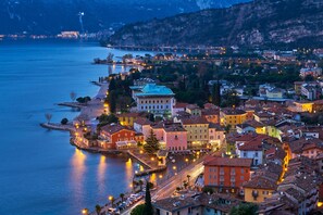 A coastal town with buildings along the waterfront, a prominent white building with a green roof, and a calm body of water. - Appartamento 30 Nodi Torbole (Nago-Torbole)