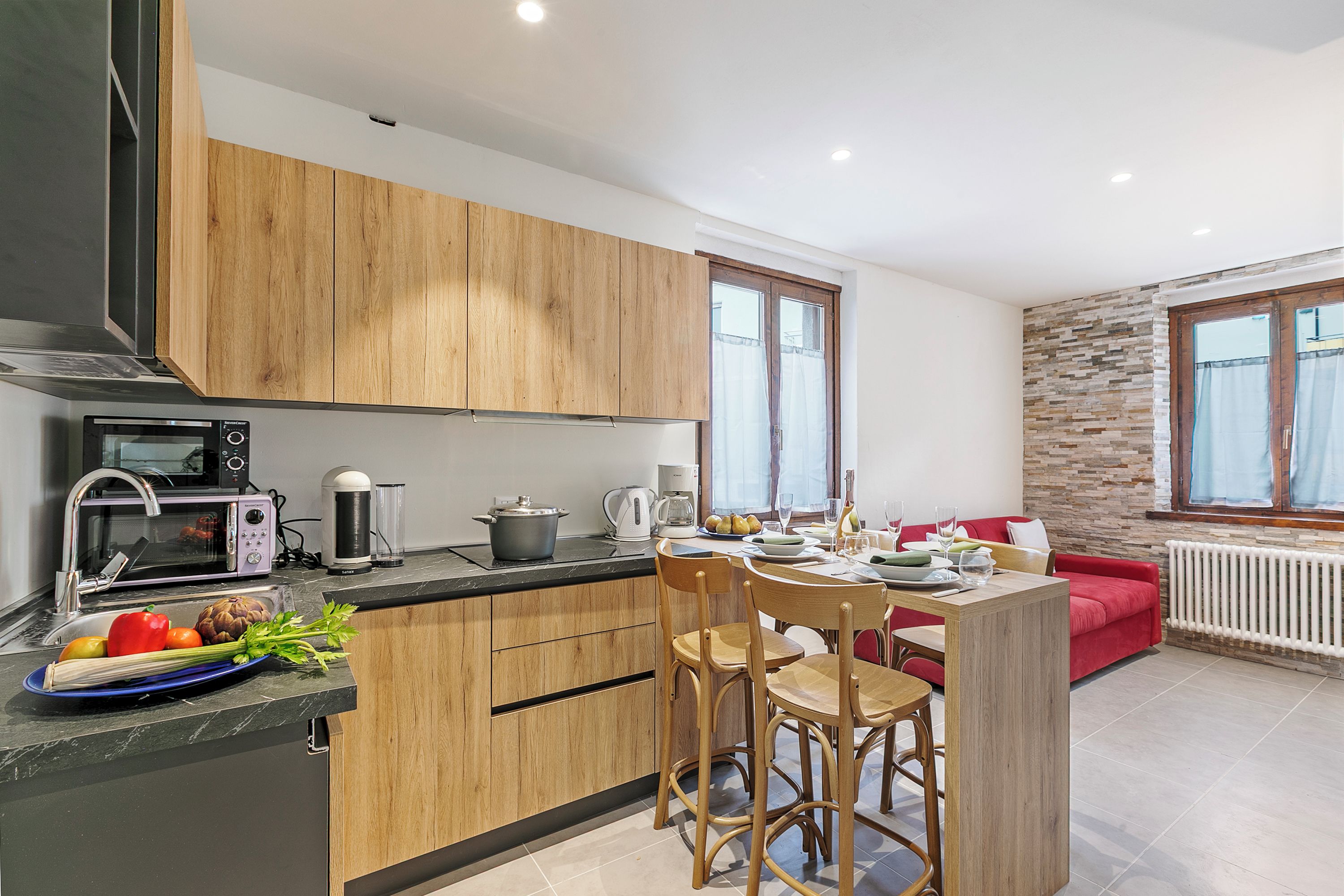 Una cocina moderna con armarios de madera, un comedor con sofá rojo y una pared de piedra.