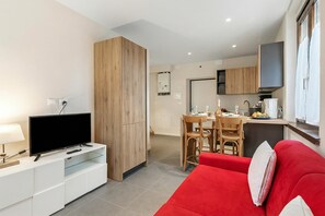 A modern living room with a flat-screen TV, a red sofa, a dining area with a table and chairs, and a kitchen area with cabinets and a countertop. - Appartamento 30 Nodi Torbole 2min Walk to Lake (Nago-Torbole)