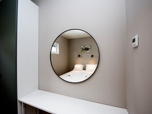 Espejo redondo en una pared, con una cama y una ventana pequeña reflejadas.