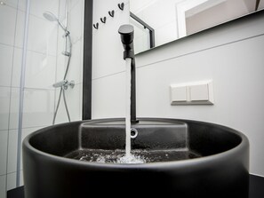Un baño moderno con un lavabo negro, un cabezal de ducha y un espejo.