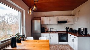 A modern kitchen with white cabinets, a wooden dining table, and a large window. - Panoramic View of Lake Harz (Clausthal-Zellerfeld)