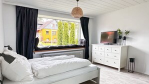 A modern bedroom with a large bed, a TV, and a window with a view of trees and buildings. - Panoramic View of Lake Harz (Clausthal-Zellerfeld)