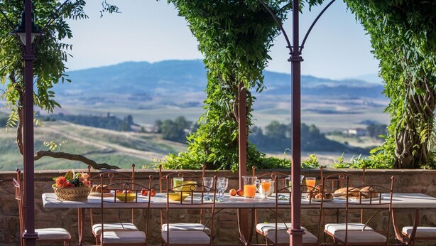 An outdoor dining area with a table set for six, surrounded by chairs, overlooking a scenic landscape. - Peccioli Villa Retreat (Peccioli)