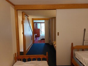 Un couloir étroit avec une porte en bois qui donne sur une chambre à coucher, où se trouvent un lit et une fenêtre.