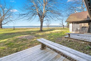 A wooden deck with benches, a stone building with a glass door, and a view of a lake. - Baileys Harbor Lakefront Abode: Waterfront Haven (Baileys Harbor)