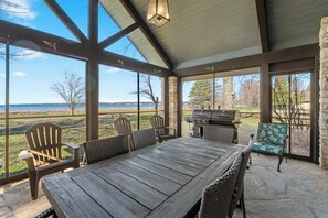 A covered patio with a wooden table and chairs, a grill, and a view of the lake. - Baileys Harbor Lakefront Abode: Waterfront Haven (Baileys Harbor)