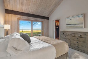 A bedroom with a bed, a dresser, a painting, and a view of the outdoors. - Baileys Harbor Lakefront Abode: Waterfront Haven (Baileys Harbor)