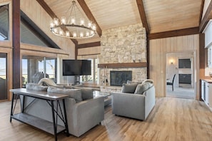A spacious living room with a stone fireplace, a large flat-screen TV, and a modern sofa set. - Baileys Harbor Lakefront Abode: Waterfront Haven (Baileys Harbor)