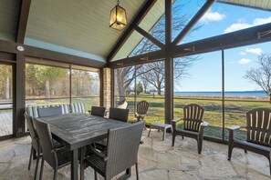 A covered patio with a table and chairs, large windows, and a view of the outdoors.