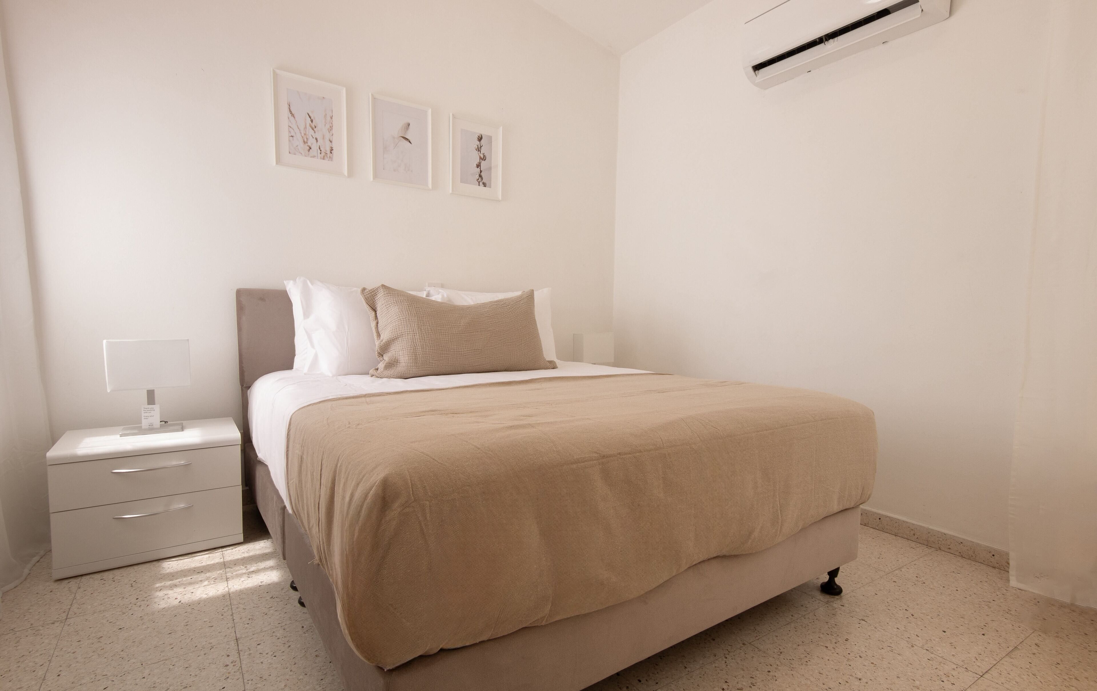Un dormitorio con una cama, una mesita de noche, una lámpara y tres cuadros en la pared.