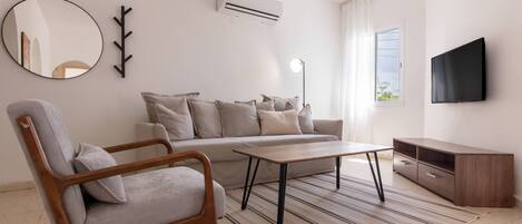 A modern living room with a sofa, a wooden chair, a coffee table, a TV, and a sideboard.
