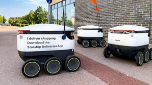 Three delivery robots parked in front of a building with a brick facade.