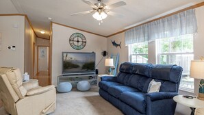 A living room with a beige sofa, a blue couch, a television, and a ceiling fan. - Poe's Paradise: Soundside 3 Bedrooms 2 Full Baths - close to beach (Emerald Isle)