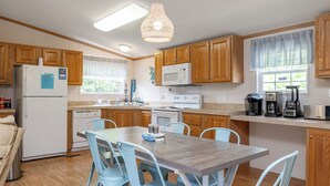 A kitchen with wooden cabinets, a white refrigerator, a microwave, a stove, and a dining table with chairs. - Poe's Paradise: Soundside 3 Bedrooms 2 Full Baths - close to beach (Emerald Isle)