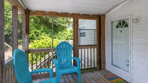 A covered porch with two blue Adirondack chairs, a wooden deck, and a white door with a window. - Poe's Paradise: Soundside 3 Bedrooms 2 Full Baths - close to beach (Emerald Isle)