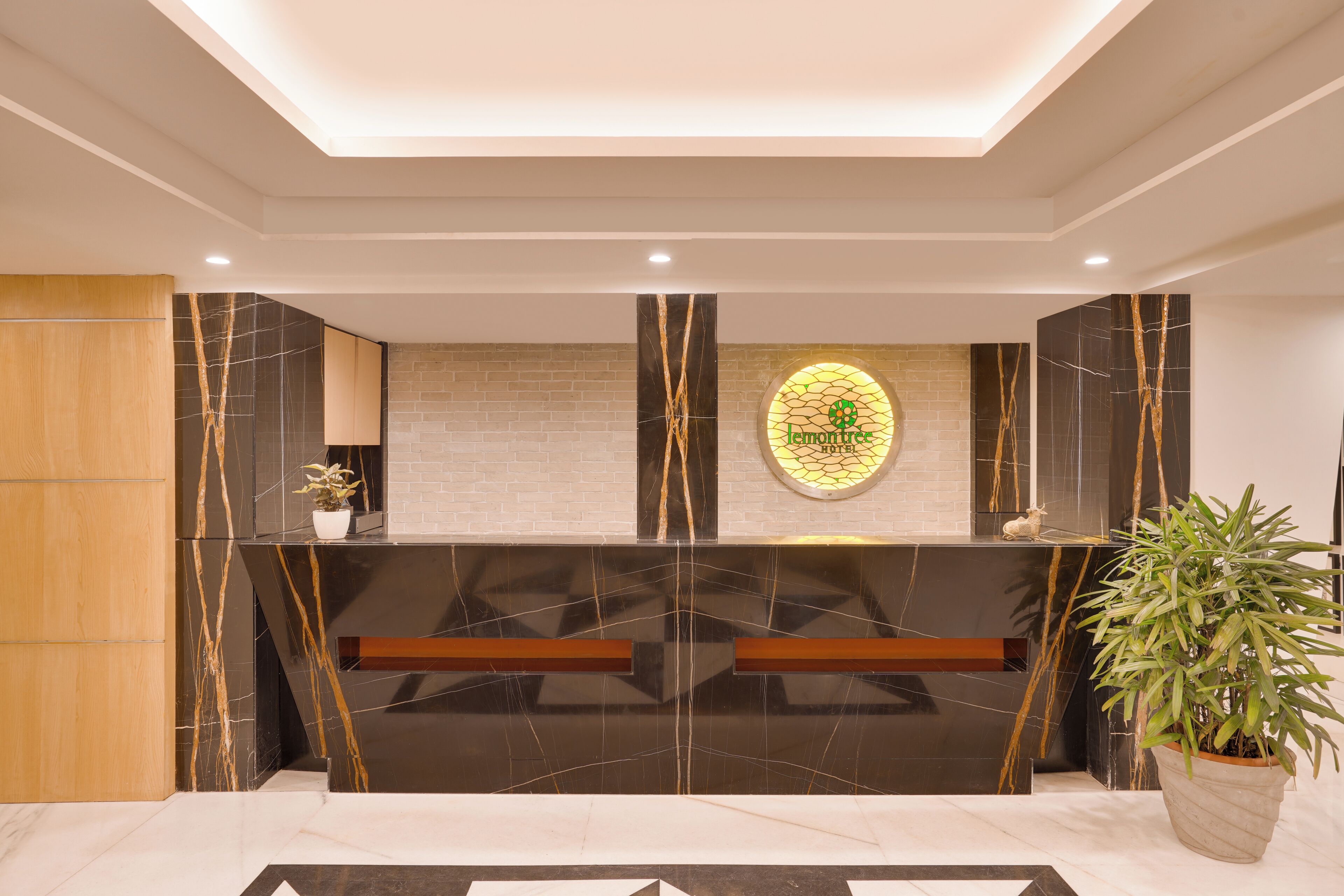 A reception area with a modern design, featuring a marble reception desk, a potted plant, and a logo on the wall.