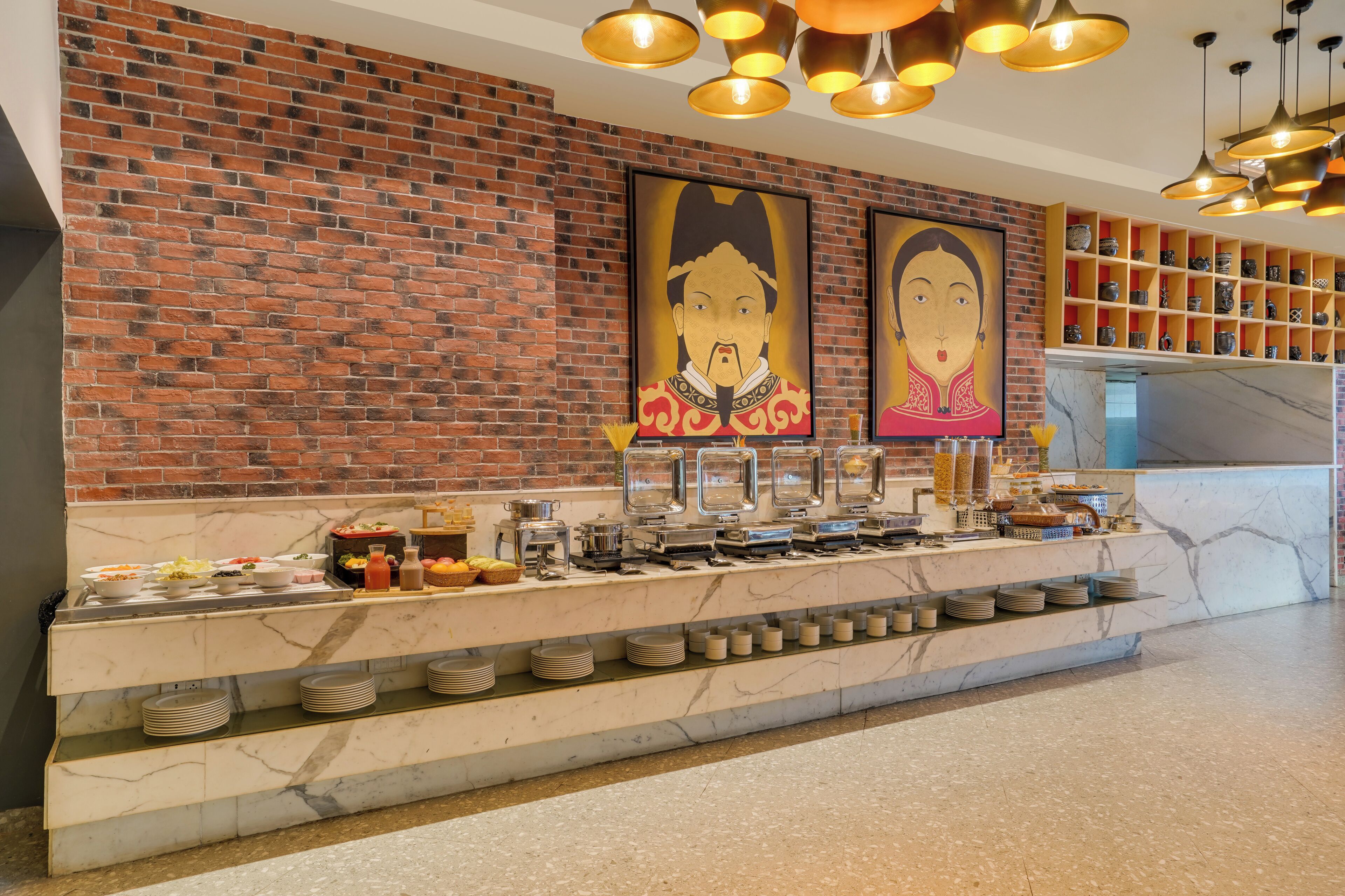 A buffet setup with a marble countertop, a brick wall, and a ceiling with hanging lights.