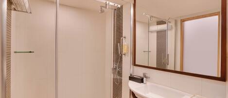 Un baño moderno con ducha de vidrio, un lavamanos blanco y un espejo grande.