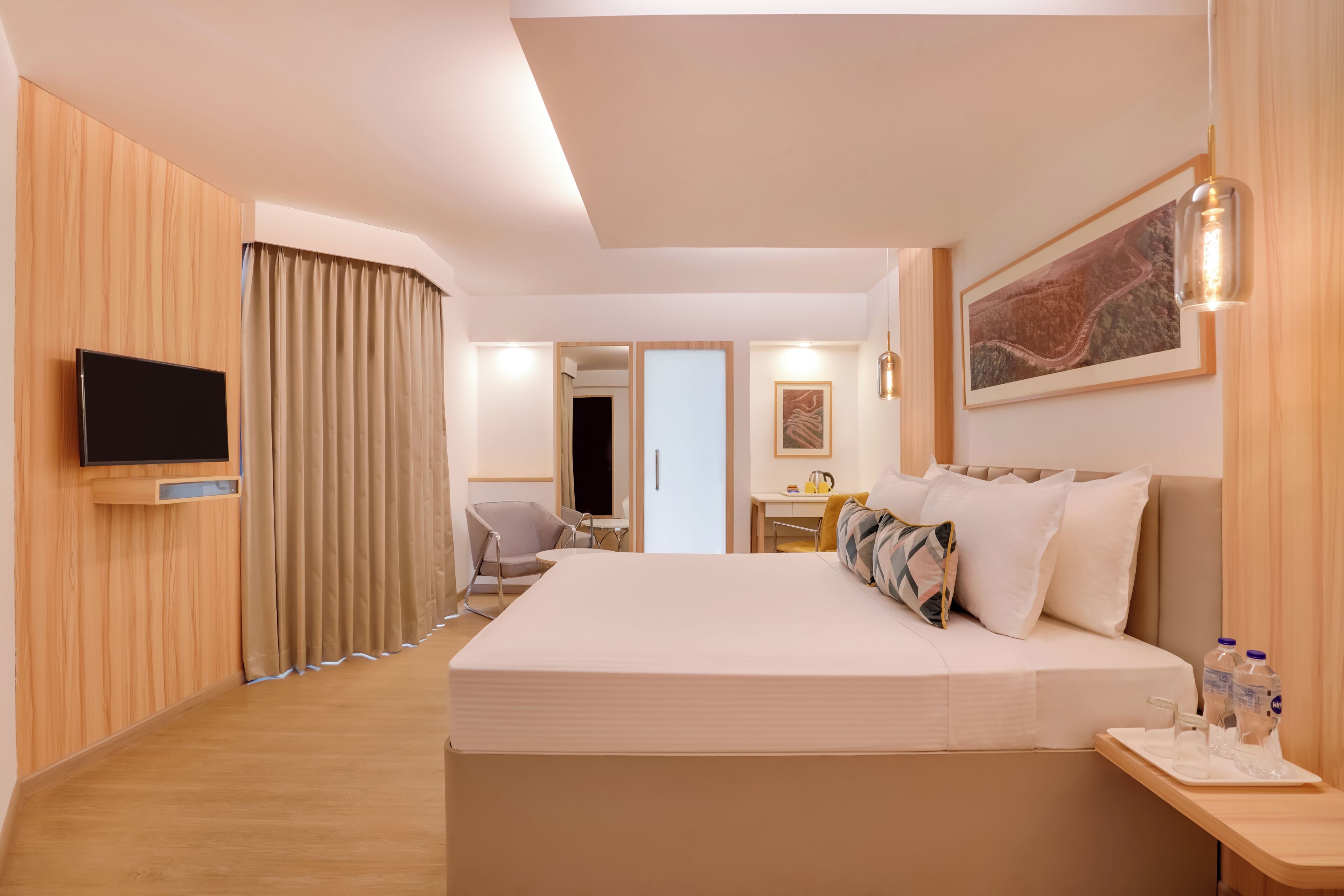 Habitación de hotel moderna con una cama grande, un televisor de pantalla plana montado en la pared, un escritorio con silla y una mesita con bandeja.