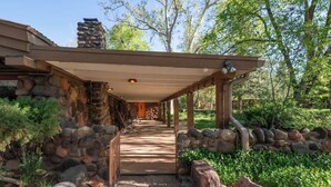 A covered outdoor area with a stone wall, a wooden deck, and a pathway leading to a building entrance. - Historic Doodlebug Ranch - A Sedona Landmark (Sedona)