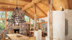 A rustic cabin interior with a stone fireplace, wooden dining table, and a large chandelier. - Historic Doodlebug Ranch - A Sedona Landmark (Sedona)