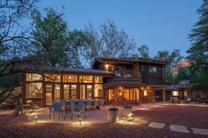 Una casa de dos plantas con fachada de piedra, un balcón y un patio con mobiliario exterior.